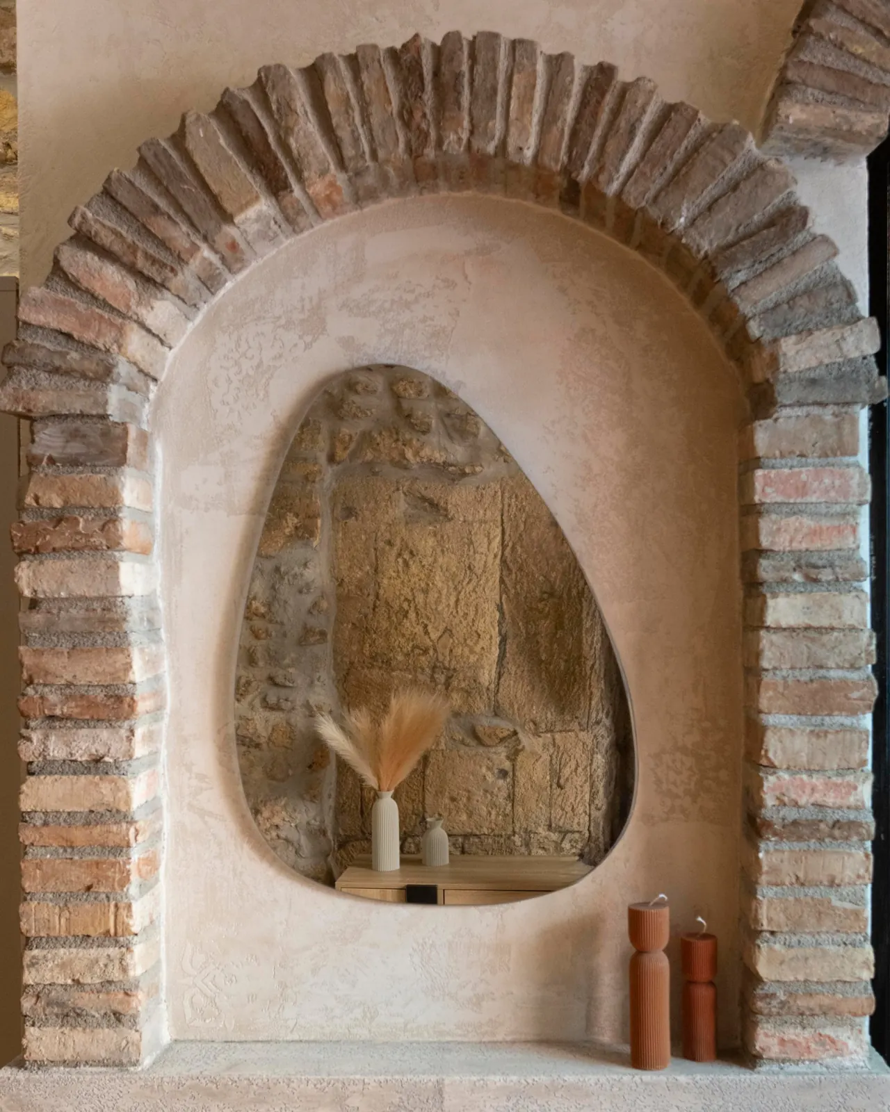 Arco in mattoni antichi con specchio sagomato, vaso con piume e candele color terracotta
