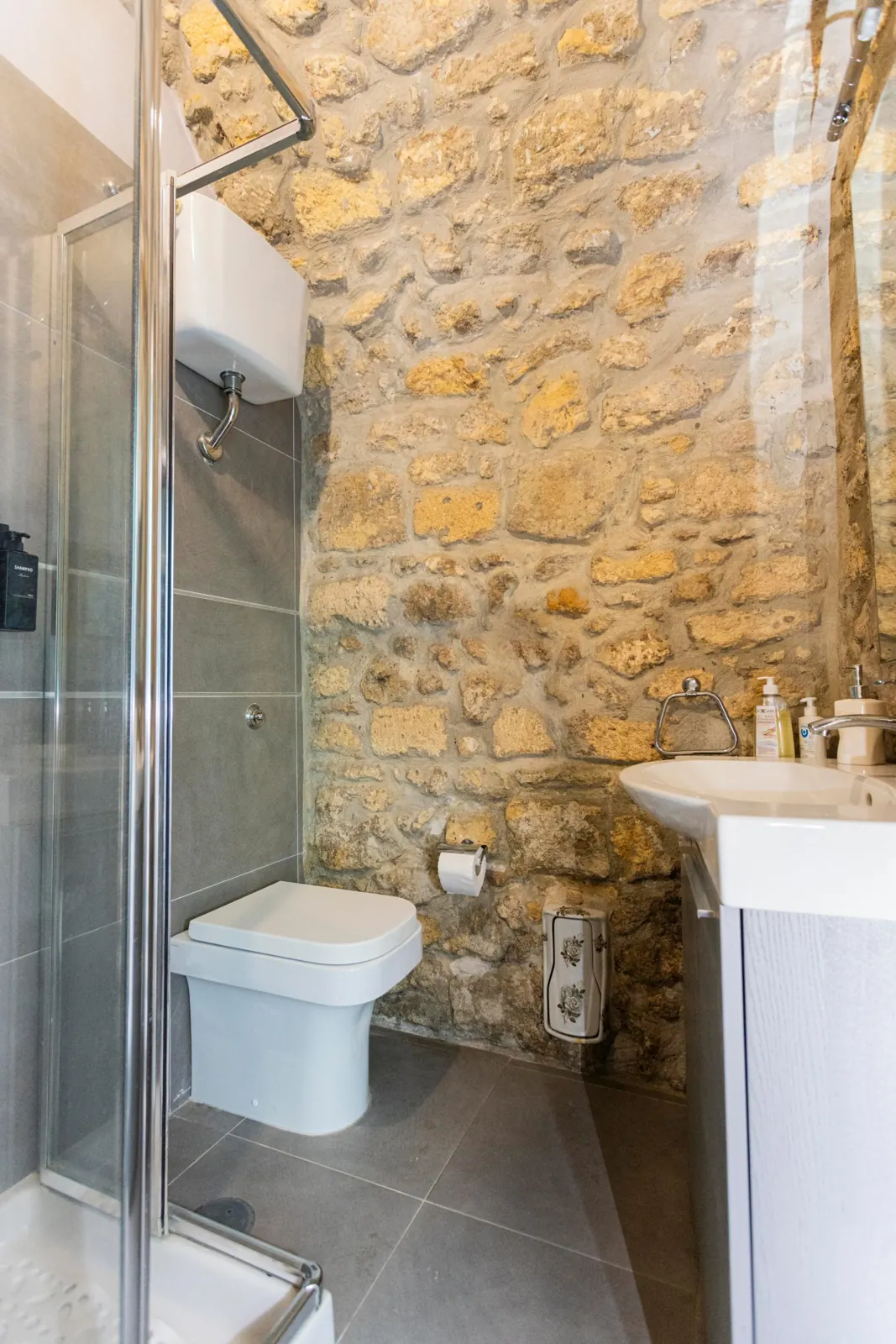 Bagno con parete in pietra a vista, doccia in vetro, lavabo con mobile e sanitari
