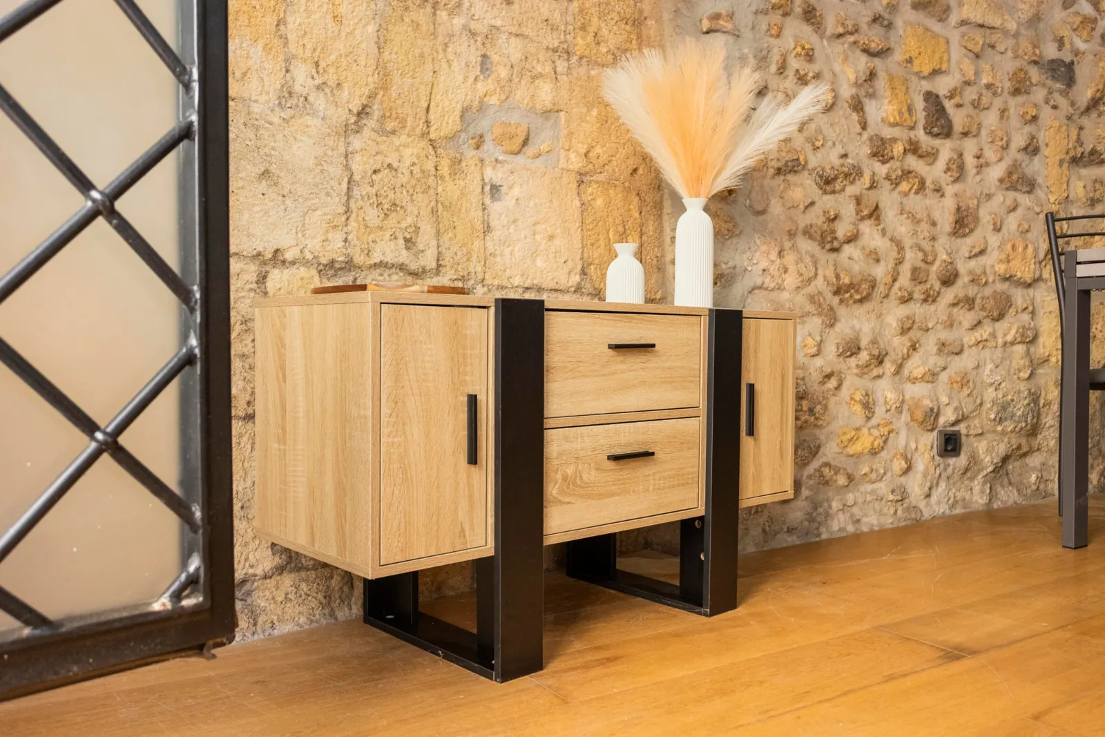 Credenza in legno e metallo con vasi bianchi e piume, accanto all'inferriata d'ingresso