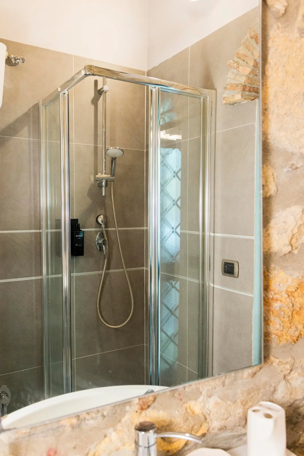 Box doccia in vetro con soffione e doccino, visto dallo specchio del bagno