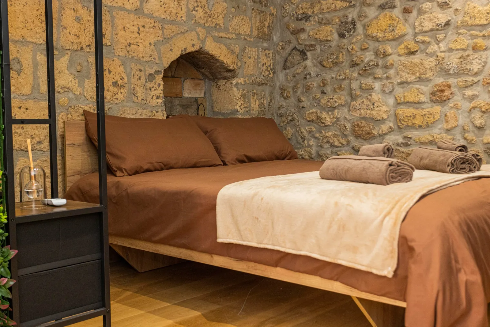 Letto matrimoniale con lenzuola marroni e plaid color sabbia davanti a una nicchia nella pietra