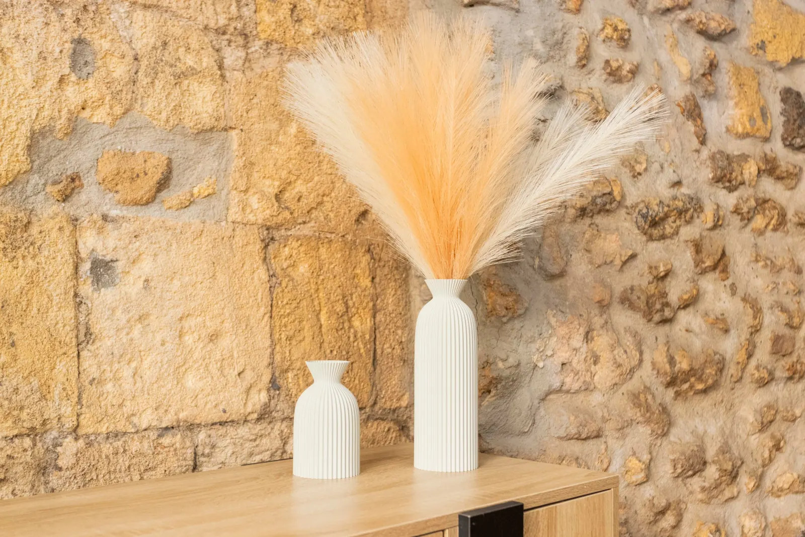 Due vasi bianchi a coste e piume color pesca su una credenza, davanti alla pietra del loft