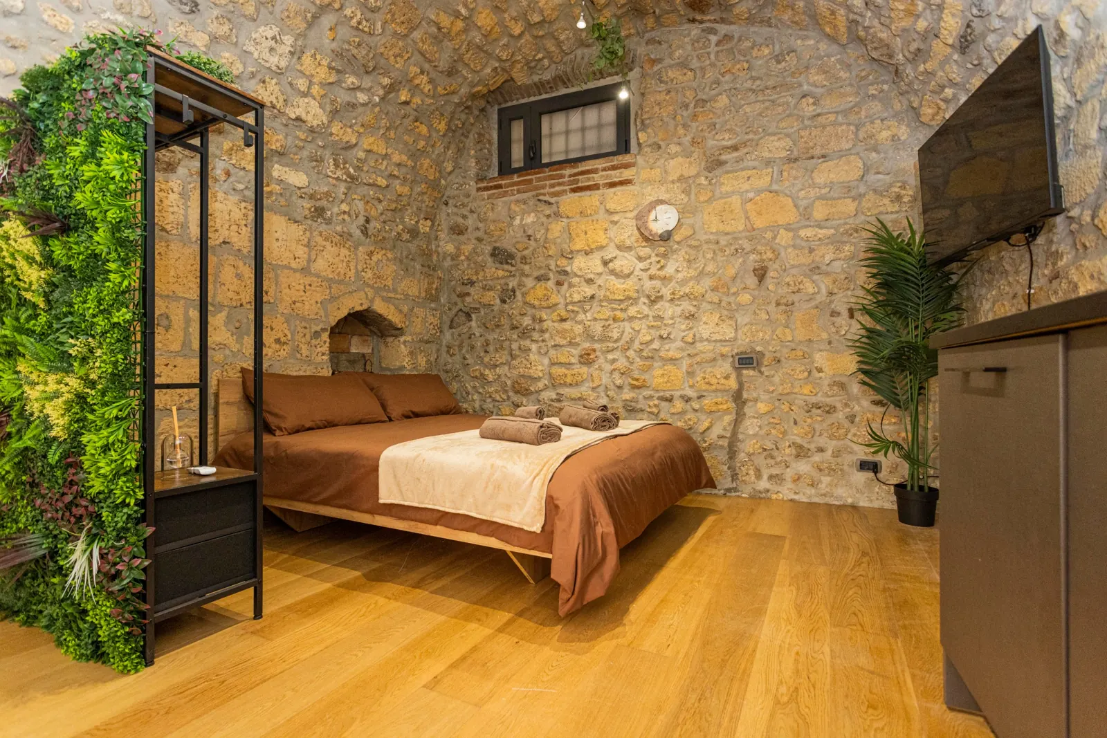 Zona notte del loft con letto matrimoniale color terracotta, parete in pietra a vista e parquet in rovere
